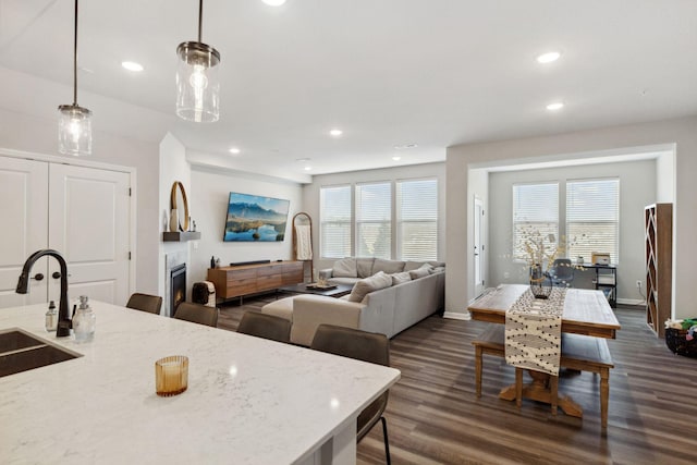 interior space with dark wood-type flooring, recessed lighting, a lit fireplace, and a sink