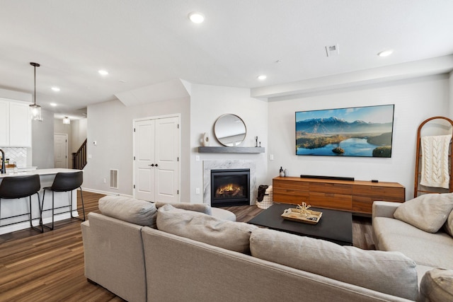 living area with visible vents, dark wood-type flooring, stairs, a premium fireplace, and recessed lighting