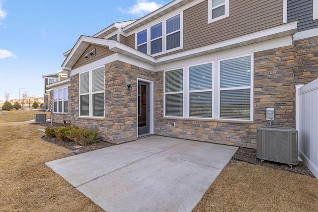 back of property featuring stone siding, a patio, and central AC