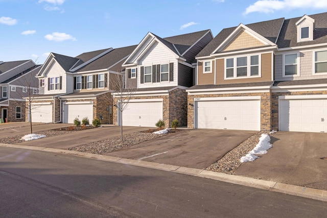 townhome / multi-family property with driveway, a garage, a residential view, and stone siding