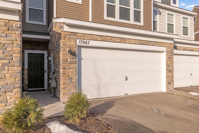 property entrance featuring stone siding, a garage, and driveway