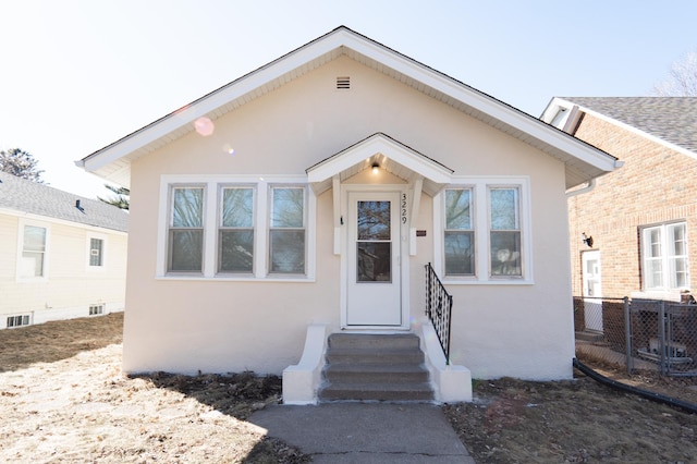 bungalow with stucco siding, fence, and entry steps