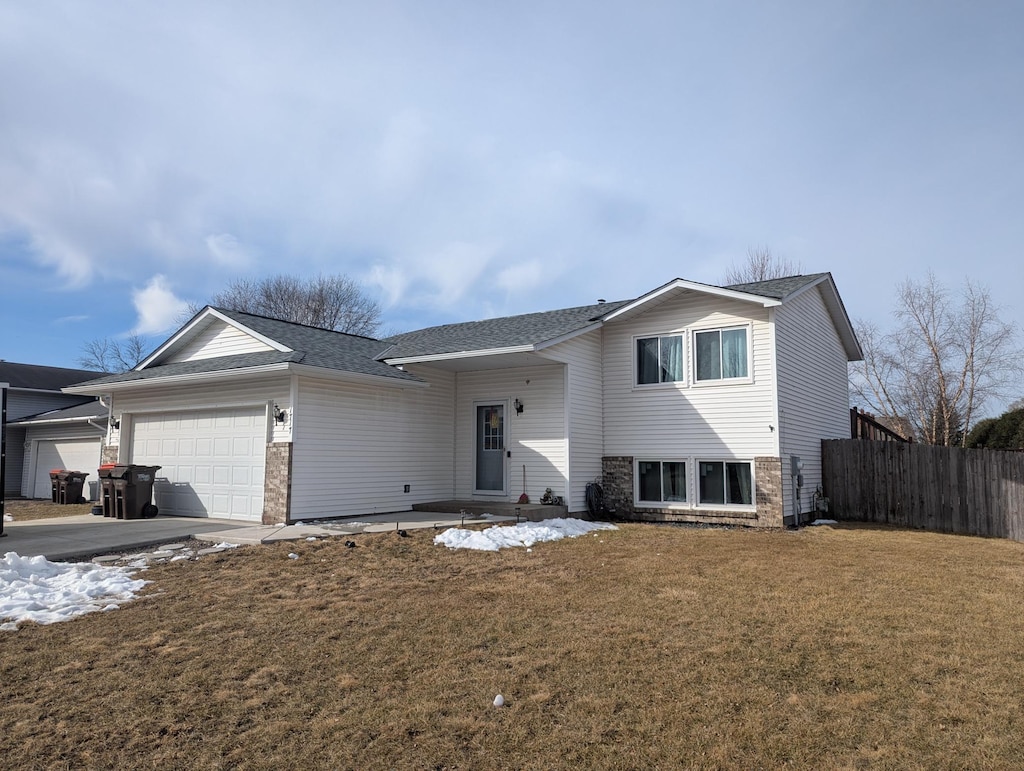 tri-level home featuring a shingled roof, a front yard, a garage, and fence