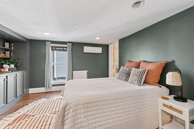 bedroom with baseboards, radiator heating unit, wood finished floors, a textured ceiling, and a wall mounted AC