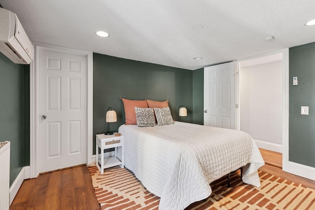 bedroom featuring an AC wall unit, a textured ceiling, wood finished floors, recessed lighting, and baseboards