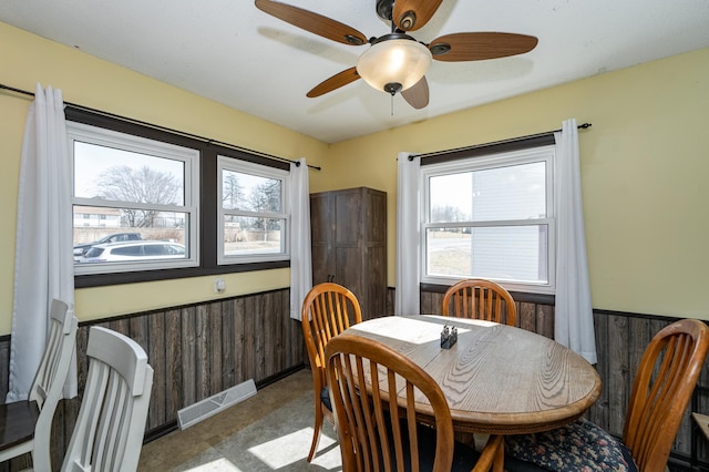 dining area featuring wooden walls, visible vents, ceiling fan, wainscoting, and tile patterned floors