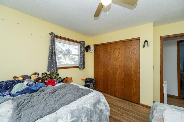 bedroom featuring baseboards, wood finished floors, a closet, a textured ceiling, and a ceiling fan