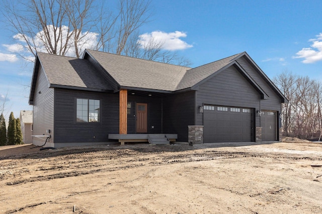 view of front facade with an attached garage, dirt driveway, and a shingled roof