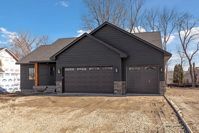 view of front of home featuring stone siding, driveway, a shingled roof, and a garage