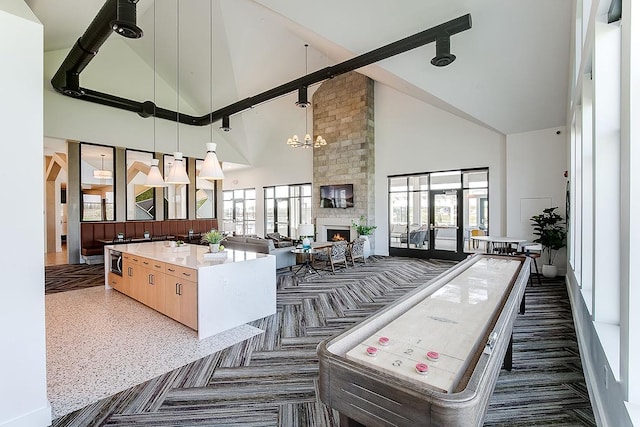 kitchen with high vaulted ceiling, light brown cabinetry, open floor plan, a large fireplace, and a chandelier