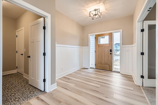 foyer featuring a wainscoted wall, a textured ceiling, and light wood-style floors