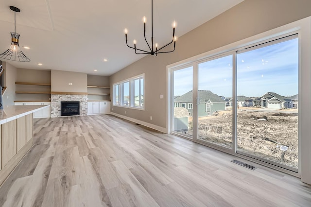 unfurnished living room featuring baseboards, visible vents, light wood finished floors, an inviting chandelier, and a fireplace