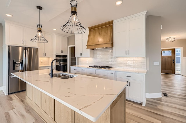 kitchen featuring light wood finished floors, premium range hood, decorative backsplash, appliances with stainless steel finishes, and a sink