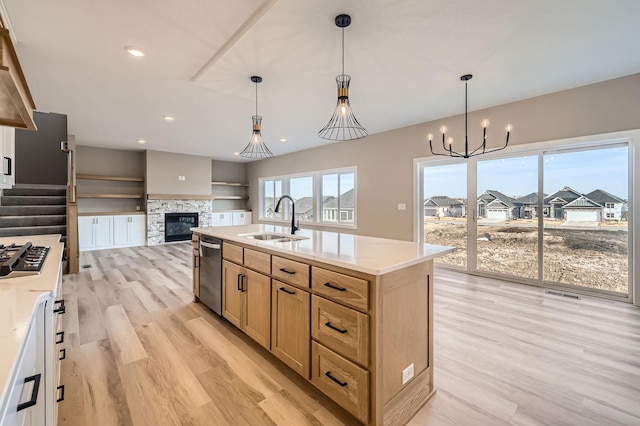 kitchen featuring light wood finished floors, a sink, appliances with stainless steel finishes, pendant lighting, and open floor plan