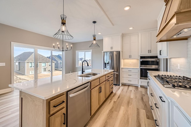 kitchen with a center island with sink, custom range hood, a sink, appliances with stainless steel finishes, and decorative backsplash