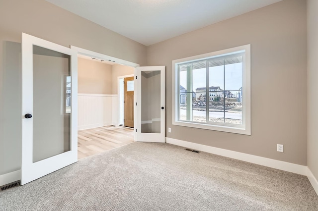 carpeted spare room featuring french doors, visible vents, and wainscoting