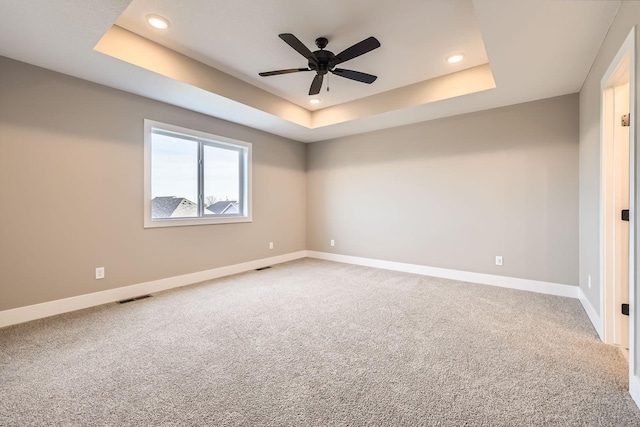 spare room featuring a raised ceiling, carpet flooring, recessed lighting, and baseboards