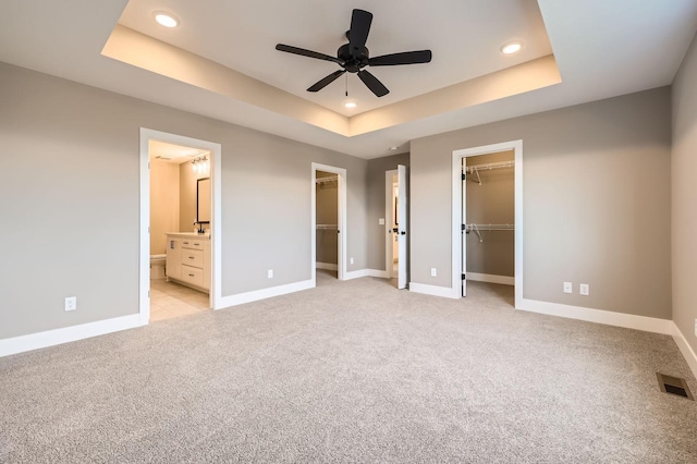 unfurnished bedroom featuring a spacious closet, visible vents, baseboards, light carpet, and a raised ceiling