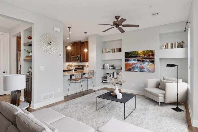 living area featuring visible vents, ceiling fan, baseboards, built in features, and wood finished floors