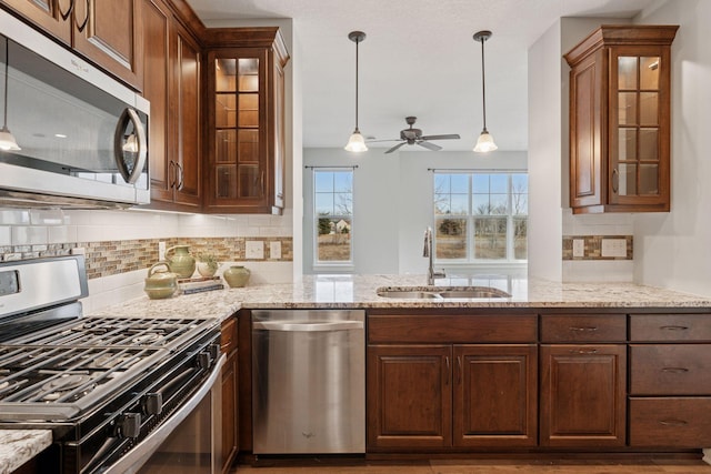 kitchen with light stone countertops, pendant lighting, a peninsula, stainless steel appliances, and a sink