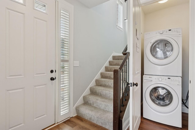 laundry room featuring laundry area, stacked washer / dryer, wood finished floors, and baseboards