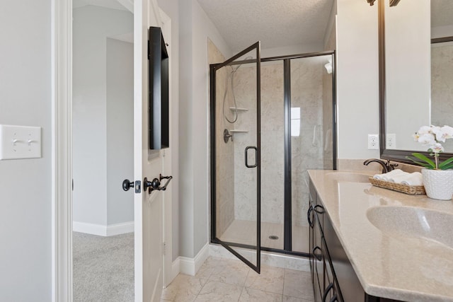 full bathroom with baseboards, double vanity, a stall shower, a textured ceiling, and a sink