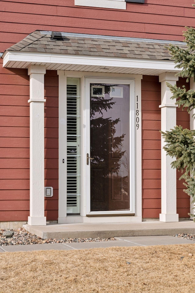 view of exterior entry featuring roof with shingles