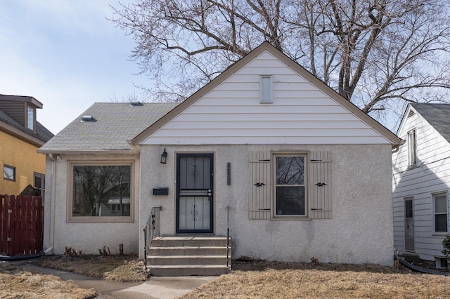 bungalow featuring stucco siding and fence