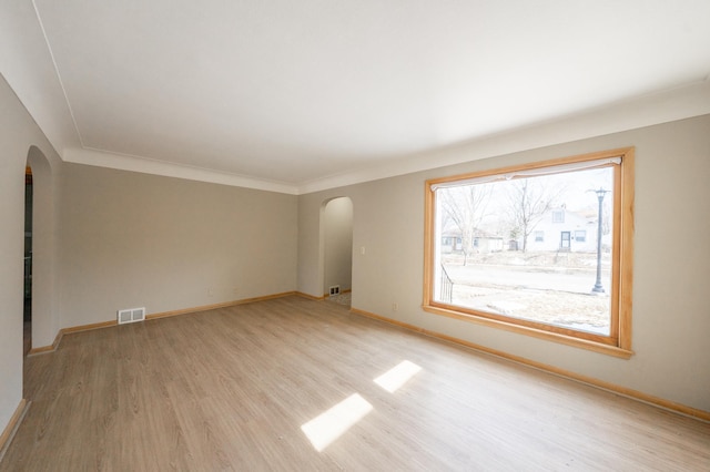 spare room featuring baseboards, visible vents, arched walkways, and light wood-type flooring