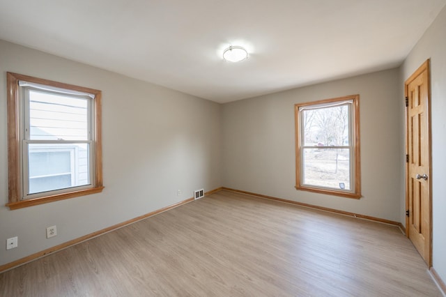 empty room with visible vents, light wood-type flooring, and baseboards