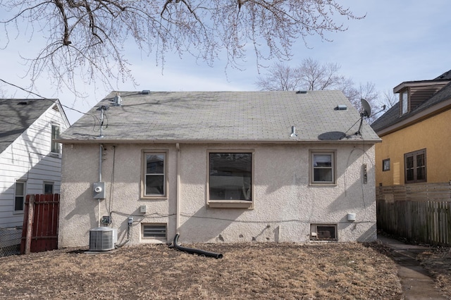 back of property with stucco siding, cooling unit, a shingled roof, and fence