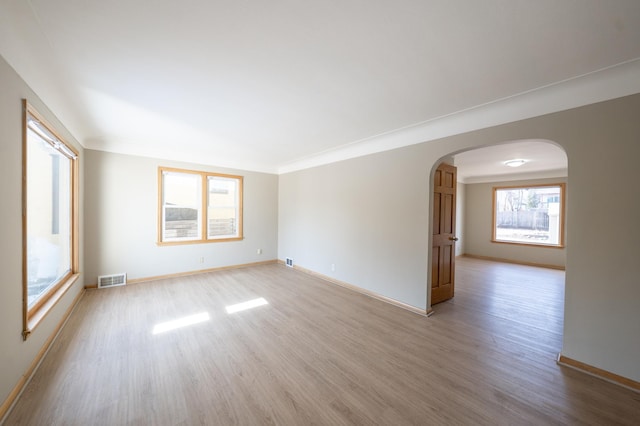 unfurnished room featuring visible vents, arched walkways, light wood-style floors, and baseboards