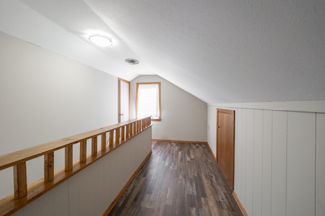 hallway featuring visible vents, a textured ceiling, dark wood-style floors, and vaulted ceiling