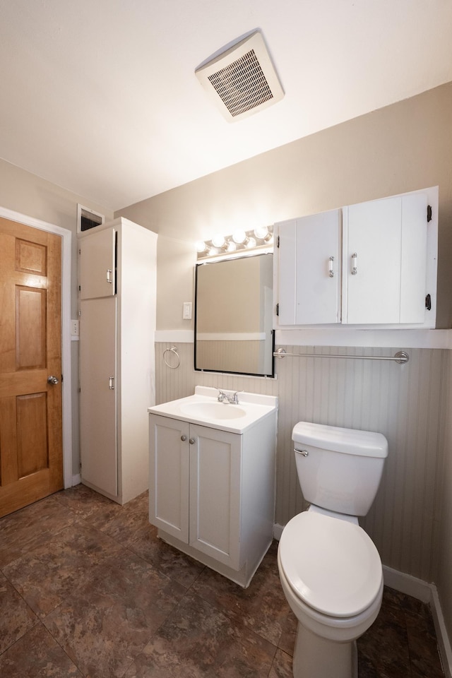 half bath featuring visible vents, toilet, vanity, and a wainscoted wall