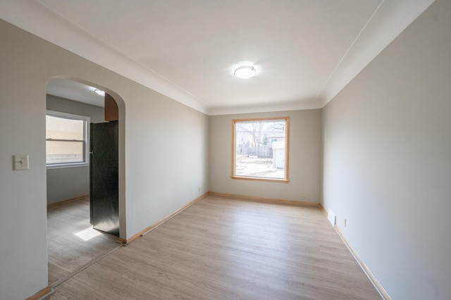 empty room with baseboards, arched walkways, and light wood-style flooring