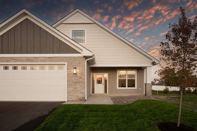 view of front of home with driveway, stone siding, a yard, board and batten siding, and a garage