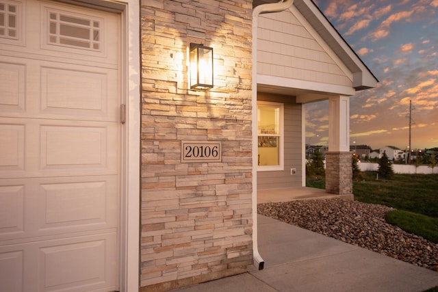 entrance to property featuring an attached garage and stone siding