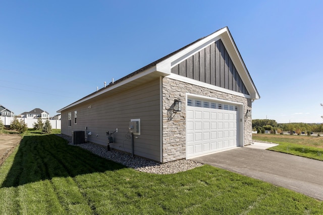 view of home's exterior with board and batten siding, central AC unit, a yard, a garage, and stone siding