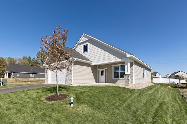 view of front of house featuring fence, driveway, an attached garage, a front lawn, and stone siding