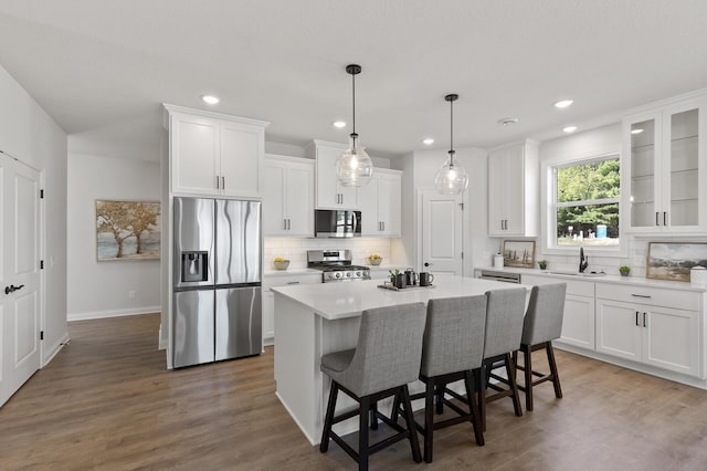 kitchen with a kitchen bar, a kitchen island, white cabinetry, stainless steel appliances, and dark wood-style flooring