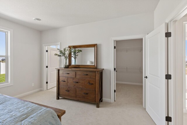 bedroom featuring a closet, baseboards, light colored carpet, and a spacious closet