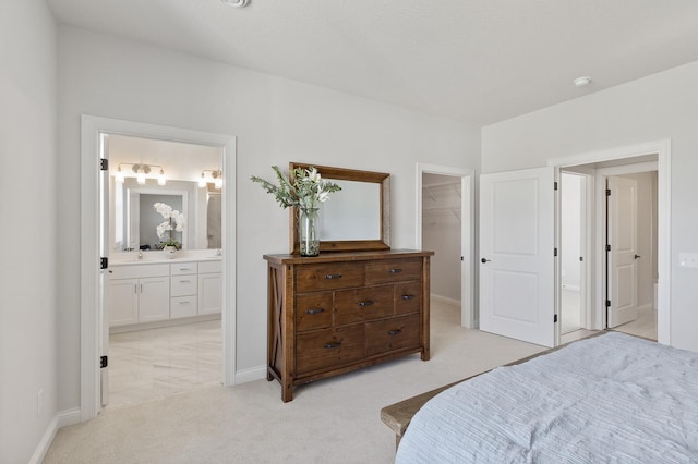 bedroom with light carpet, a spacious closet, ensuite bath, and baseboards