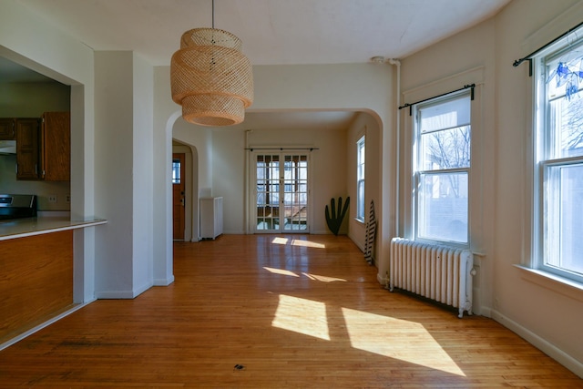 unfurnished dining area with arched walkways, light wood-style flooring, and radiator heating unit