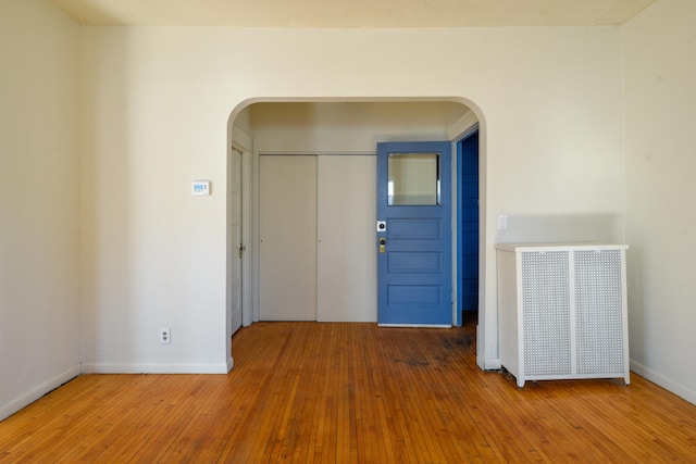 foyer entrance with arched walkways, baseboards, and wood-type flooring