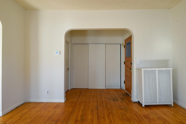 unfurnished room with hardwood / wood-style flooring, baseboards, and arched walkways