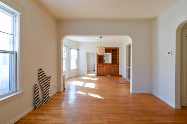 interior space with baseboards, arched walkways, and light wood-type flooring