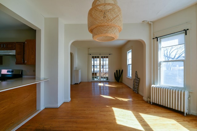 hallway with arched walkways, radiator heating unit, and light wood finished floors