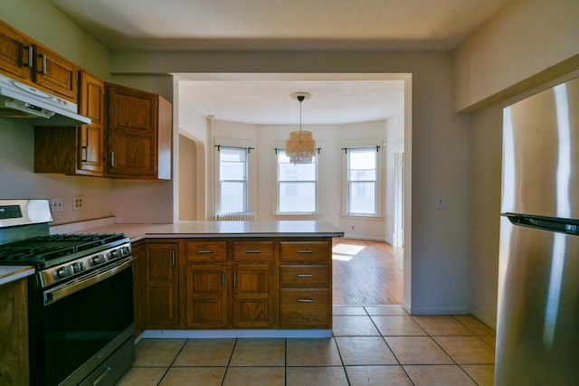 kitchen featuring under cabinet range hood, stainless steel appliances, a peninsula, light countertops, and light tile patterned floors