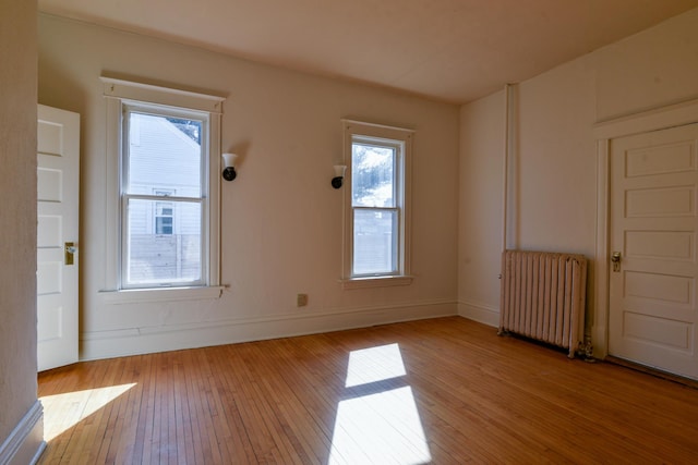 unfurnished room featuring radiator heating unit, baseboards, and wood-type flooring