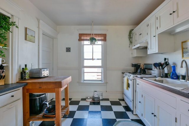 kitchen featuring white cabinets, under cabinet range hood, wainscoting, dark floors, and white gas range